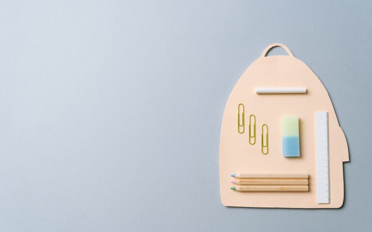 Minimalist top view of school supplies creatively arranged on a backpack-shaped platform.