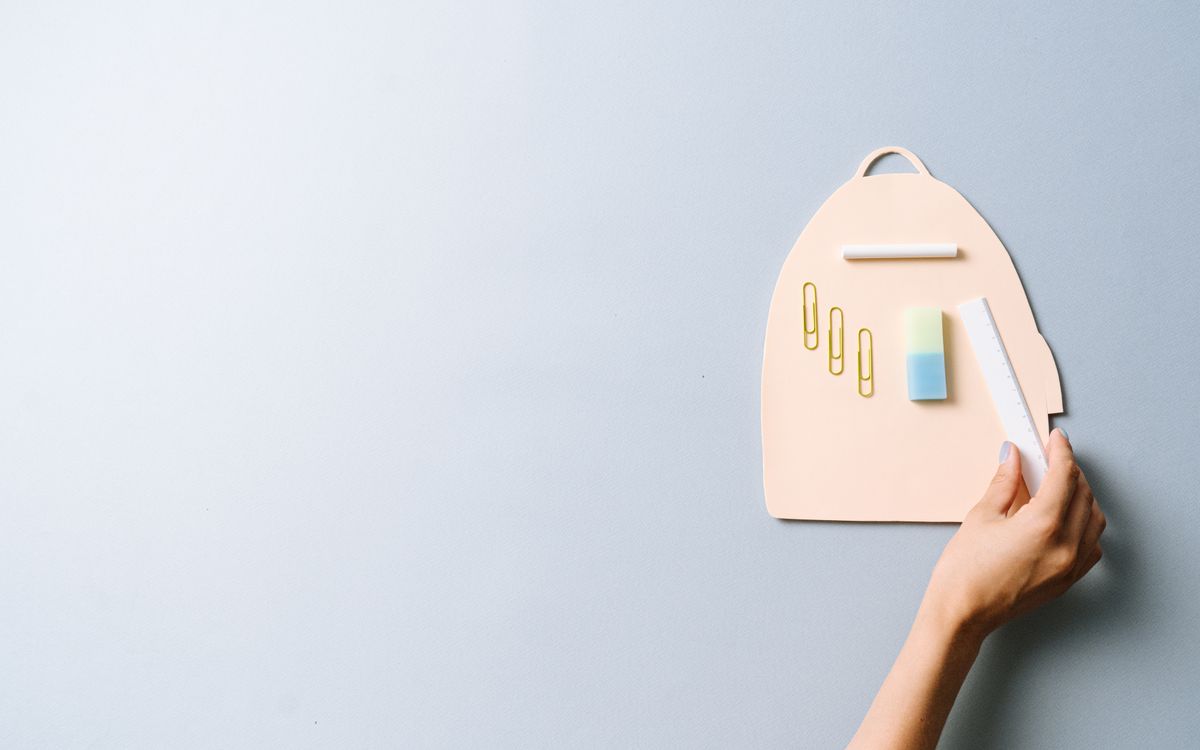 A minimalist flat lay of school supplies including a hand holding a ruler on a pastel background.