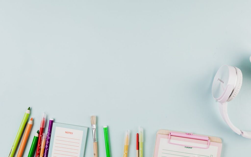 Flat lay of colorful stationery and white headphones on a blue background, ideal for creative projects.