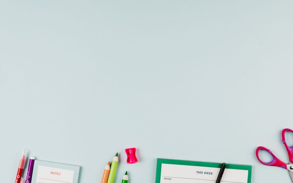 Flat lay of school supplies including colored pencils, scissors, and a notepad on a light blue background.
