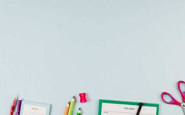 Flat lay of school supplies including colored pencils, scissors, and a notepad on a light blue background.