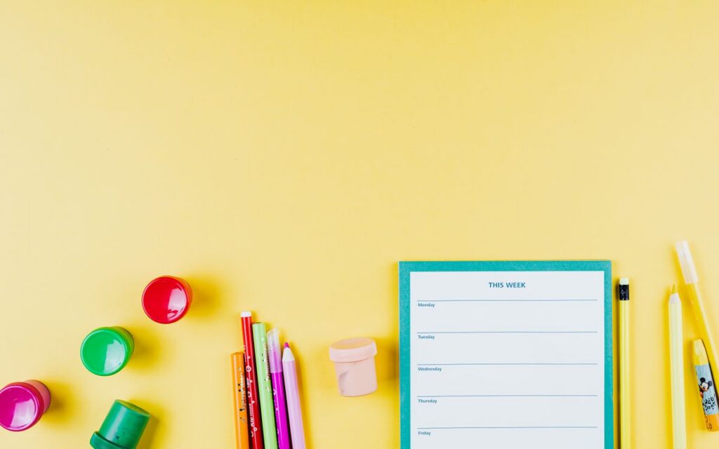 Flat lay of colorful school supplies on a yellow background with planner