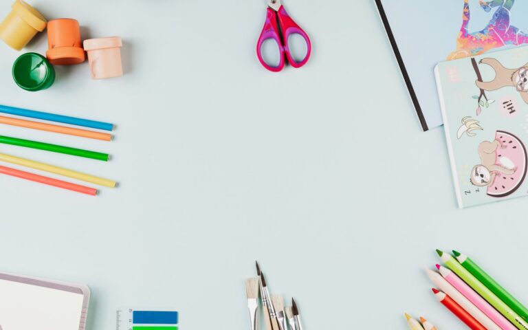 A creative flat lay of colorful art supplies arranged on a light blue background with copy space.