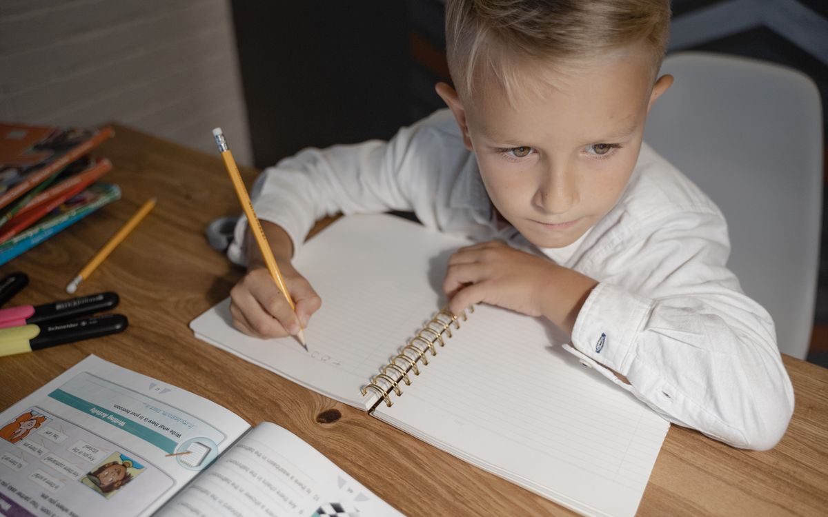 Child focused on homework, writing in a notebook with study materials nearby.