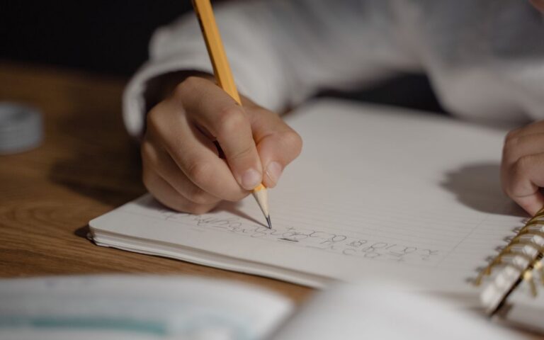 Close-up of a child writing homework using a pencil on a spiral notebook. Ideal for education themes.