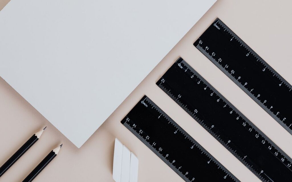 A neatly arranged flat lay of pencils, rulers, and paper on a beige background.
