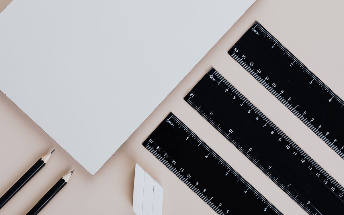 A neatly arranged flat lay of pencils, rulers, and paper on a beige background.
