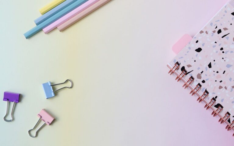 Stylish flat lay of pastel stationery with a notebook and paper clips on a soft background.