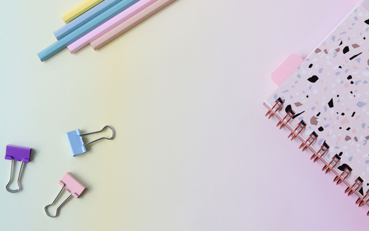 Stylish flat lay of pastel stationery with a notebook and paper clips on a soft background.