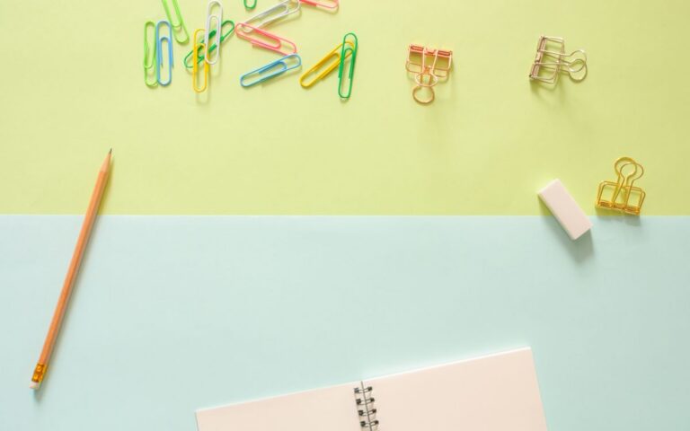 Top view of colorful stationery items, including a notebook, pencil, paperclips, and an eraser on pastel background.