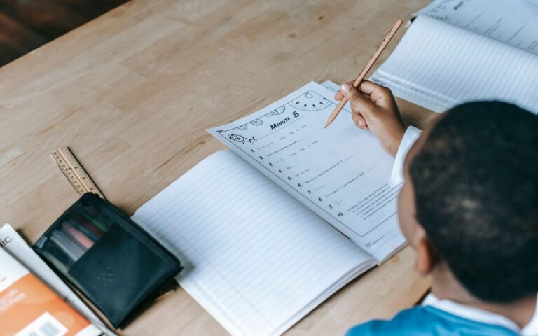 From above crop unrecognizable African American schoolboy doing test assignment while sitting at desk in light classroom