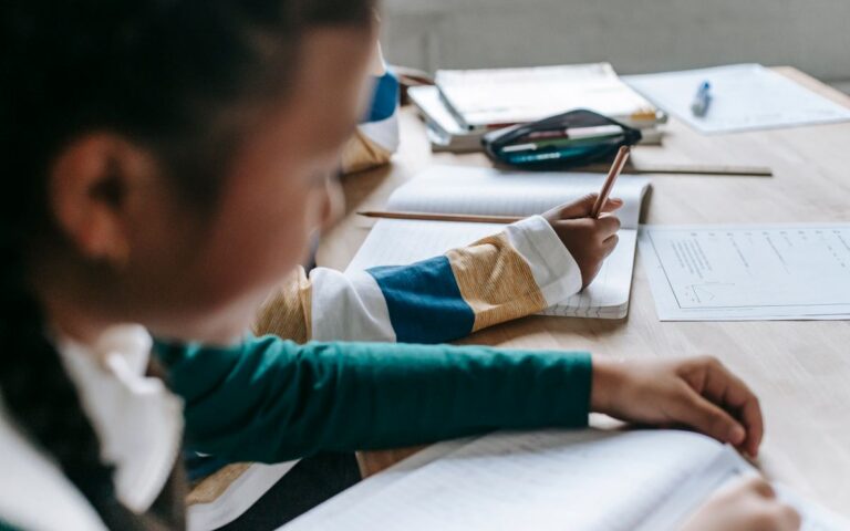 Side view crop pupils sitting at desk with notebooks while attending lesson in classroom
