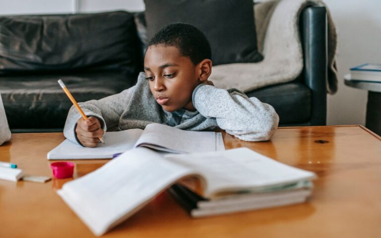 Focused African American boy writing in copybook with pencil while doing homework at wooden table