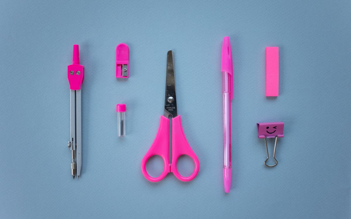 Flat lay of vibrant pink school supplies on a baby blue background, including scissors, pen, and compass.