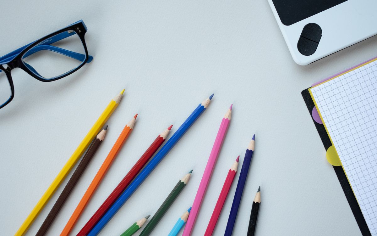 A flat lay of colorful pencils, eyeglasses, and a notepad on a desk, perfect for school themes.