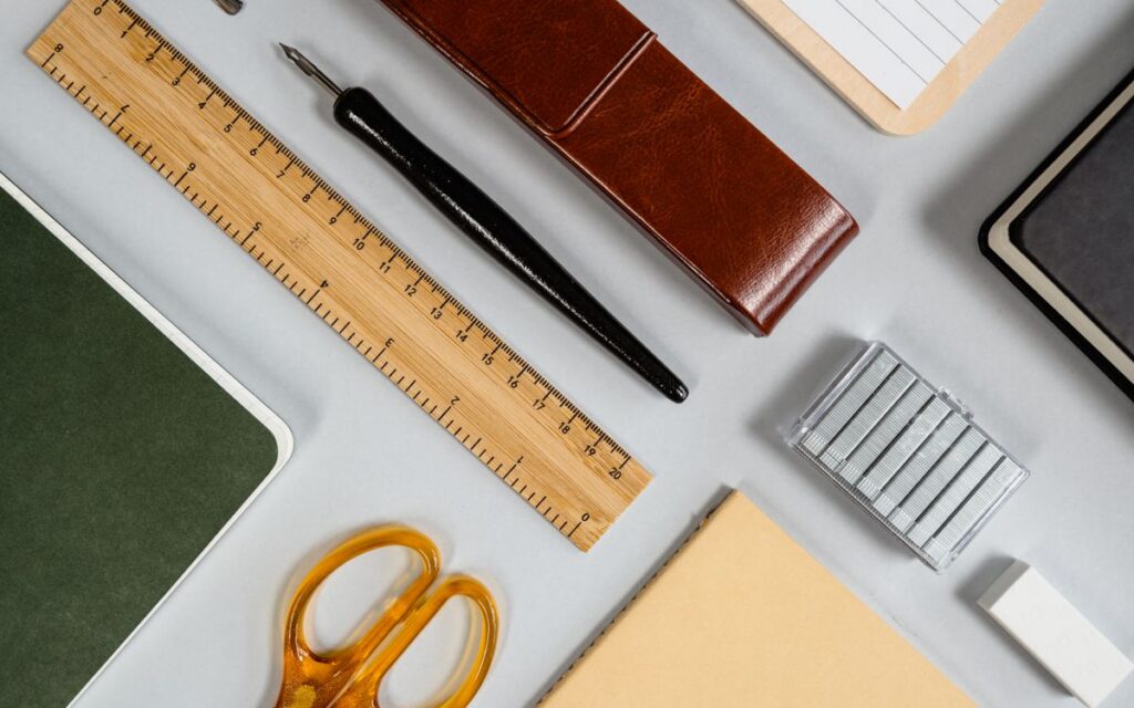 A variety of stationery including scissors, ruler, and notebook arranged in an organized flat lay on a desk.