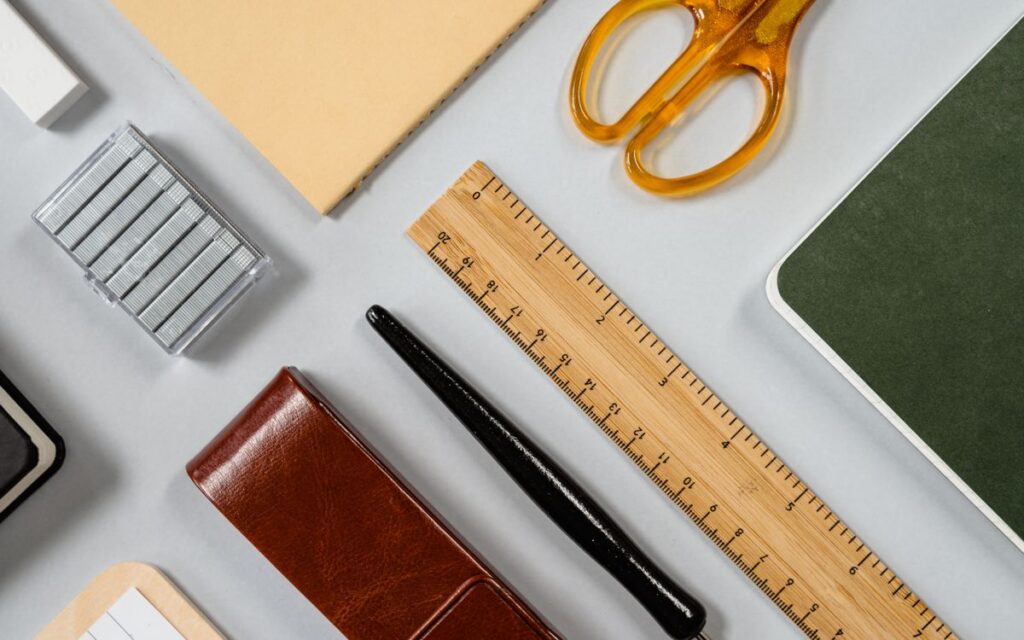 A neatly arranged flat lay of office supplies including scissors, ruler, fountain pen, and notebooks.