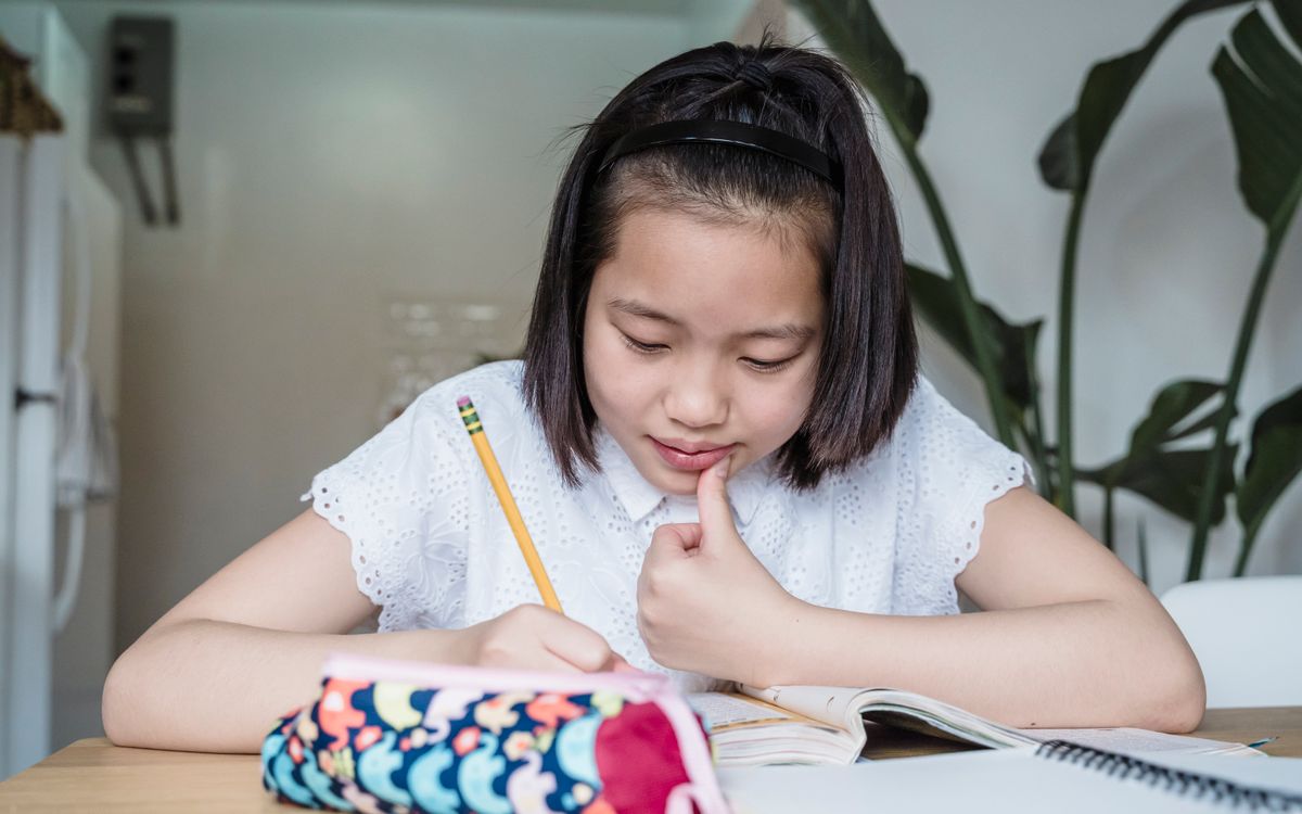 A young girl focuses on her homework while seated at a desk inside a cozy home setting.