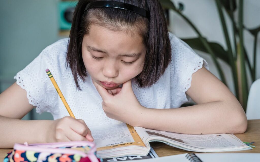 A young girl deeply engaged in homework, writing in a notebook at home.