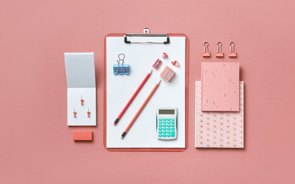 A modern flat lay of various office supplies arranged neatly on a pink background.