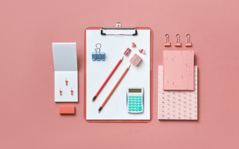 A modern flat lay of various office supplies arranged neatly on a pink background.