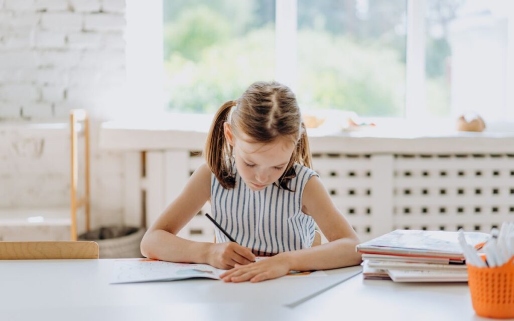 A young girl engaged in coloring at a desk indoors. Bright natural lighting.