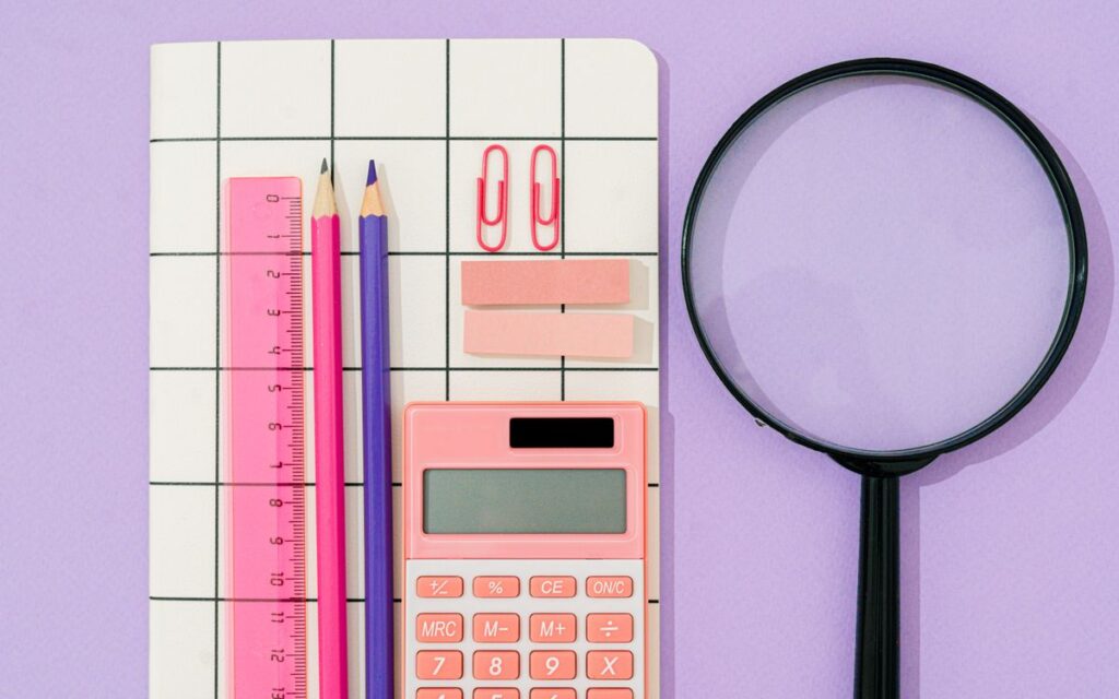 Flat lay of pastel office supplies on a grid notebook with purple background.