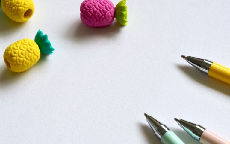 Vibrant pens and pineapple-shaped erasers on a white desk create a playful workspace ambiance.