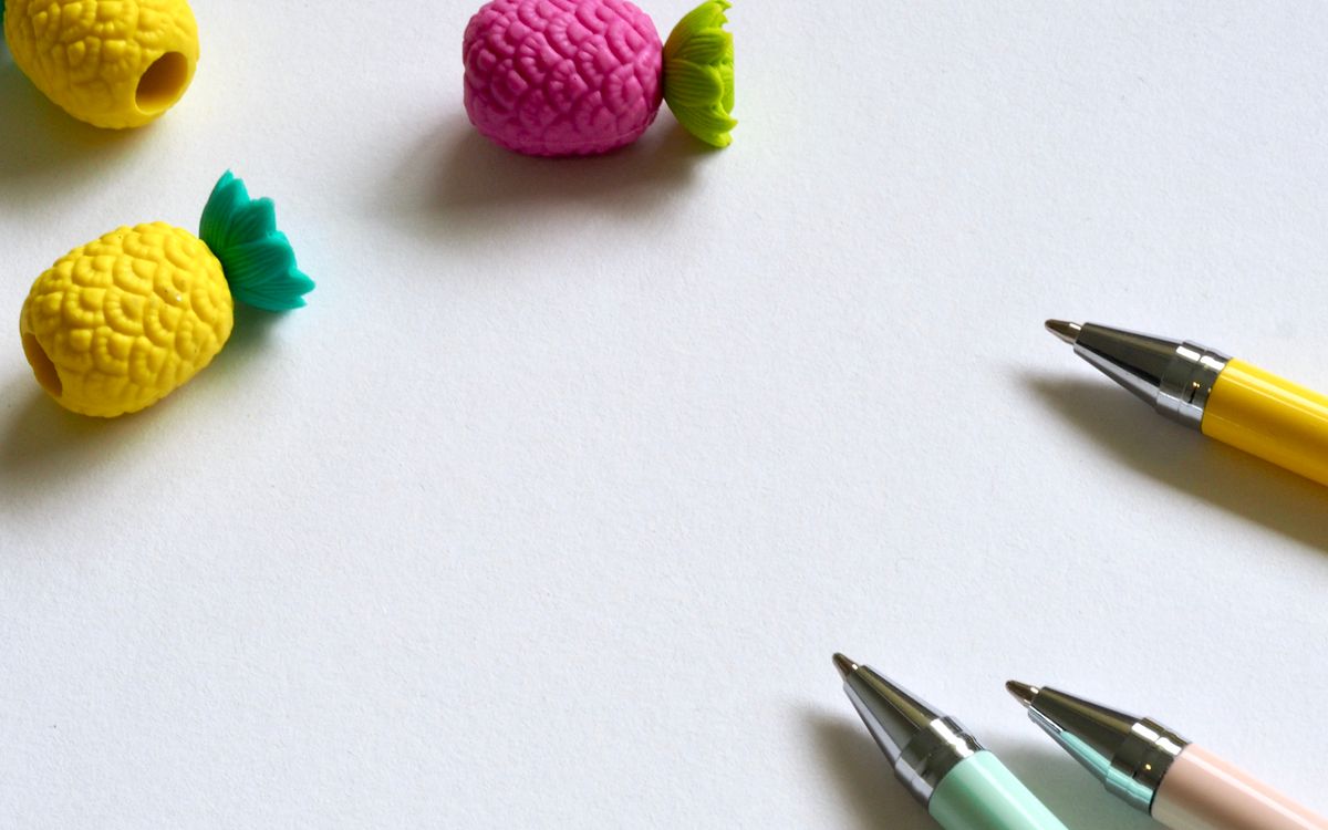 Vibrant pens and pineapple-shaped erasers on a white desk create a playful workspace ambiance.