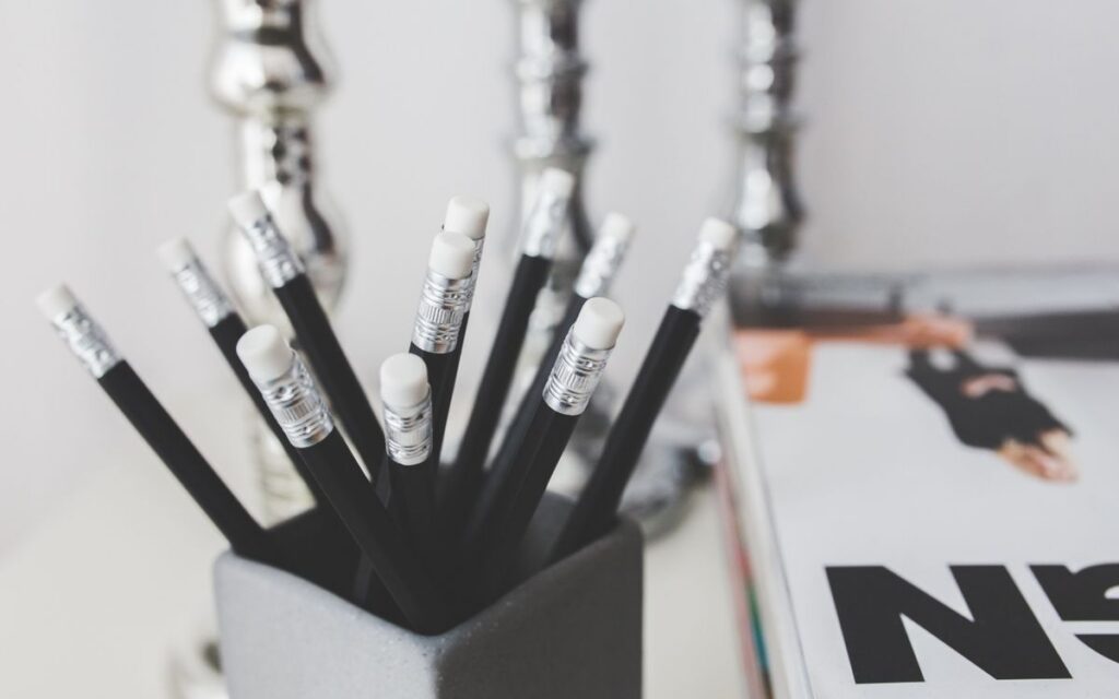 Black pencils with erasers in a holder on a minimalistic desk setup.