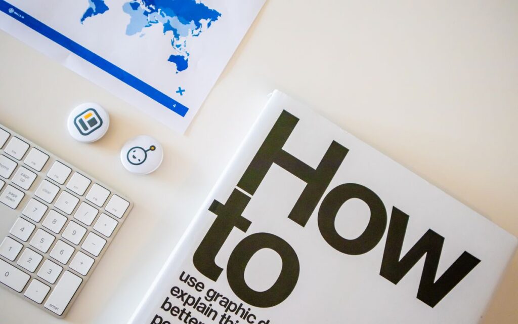 Stylish desk setup with a how-to book, keyboard, and world map on paper.