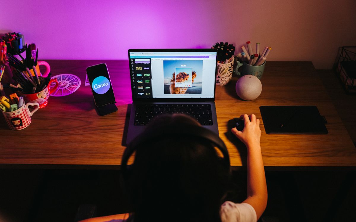 A young girl using a laptop for design work at a colorful home desk setup.