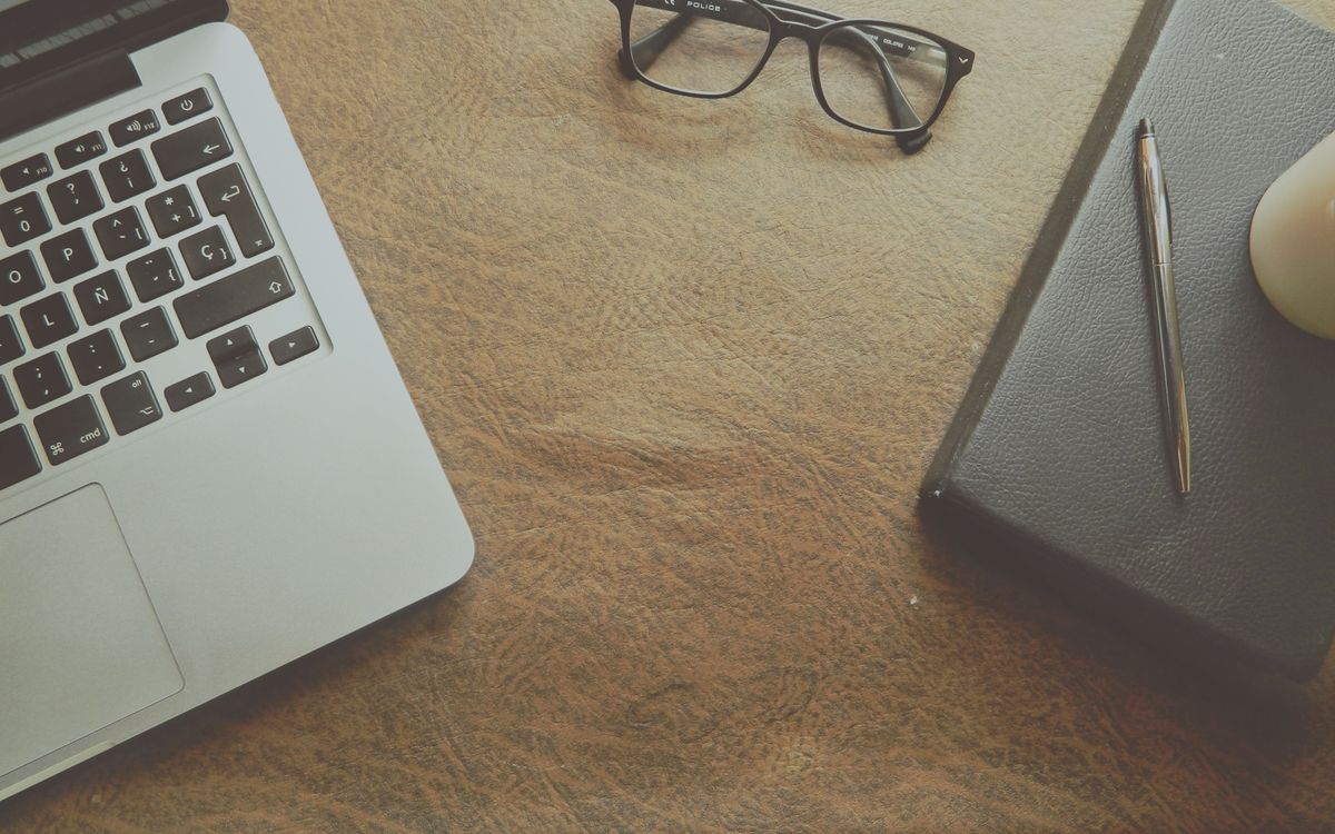 A well-organized workspace featuring a laptop, notebook, and glasses on a leather surface.