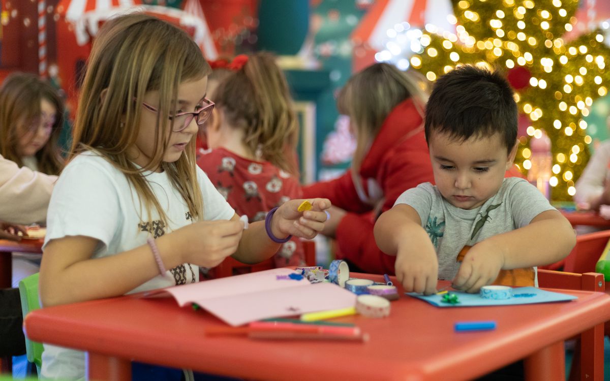 Kids creating festive crafts in a colorful, Christmas-themed classroom setting, focused on holiday creativity.