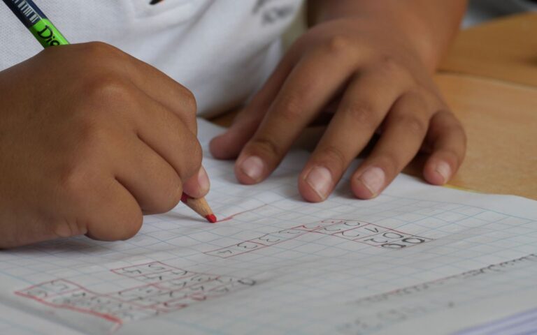 Close-up of a student writing math equations in a notebook with a pencil indoors.