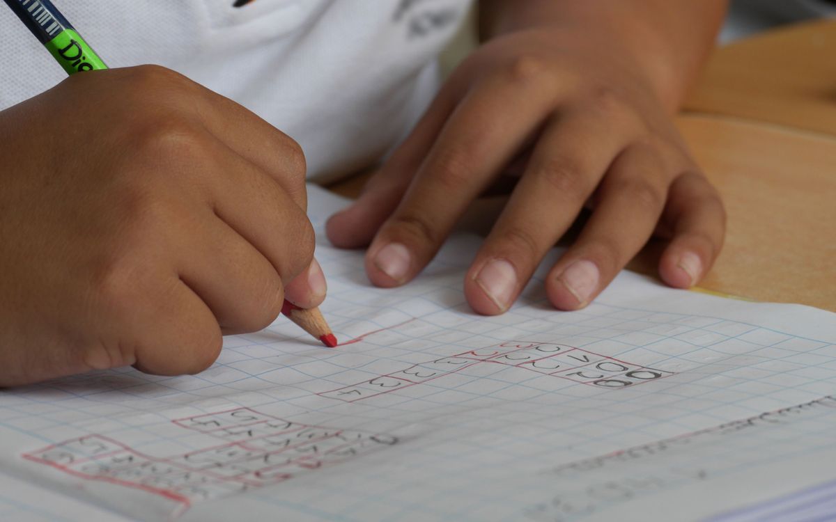 Close-up of a student writing math equations in a notebook with a pencil indoors.
