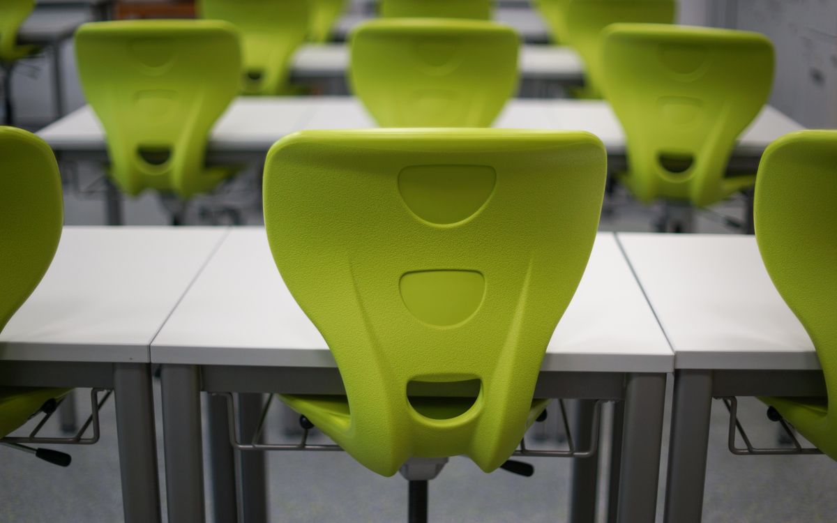 An empty modern classroom featuring rows of vibrant green plastic chairs and white desks.