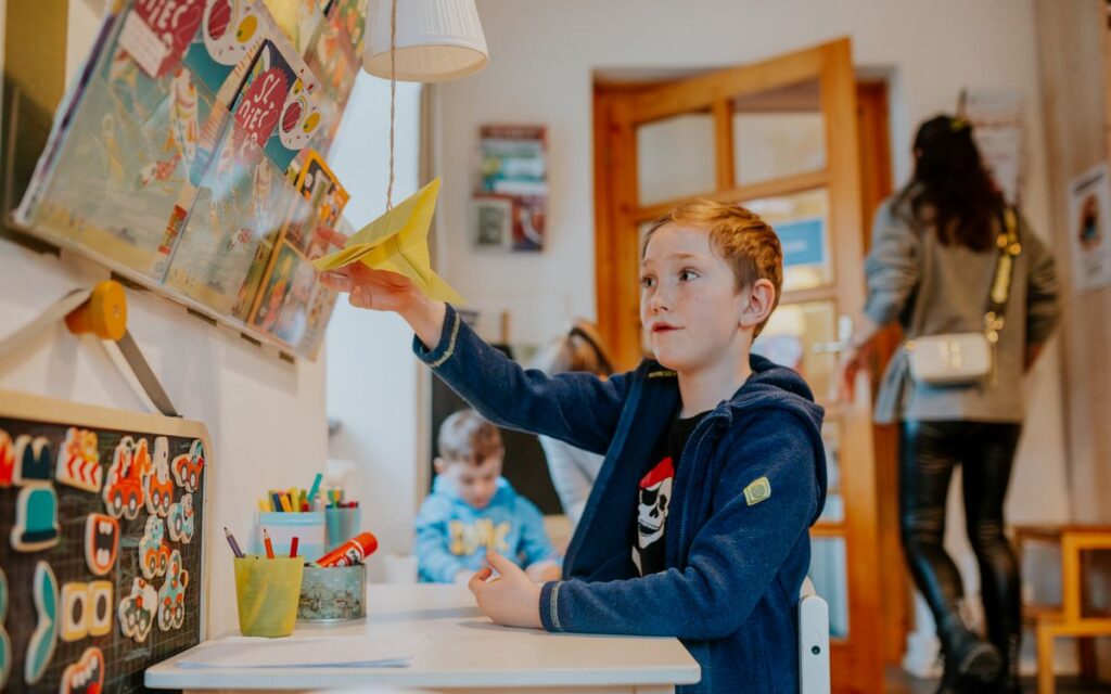 A young boy enjoying a creative activity with a paper airplane in a lively classroom setting.