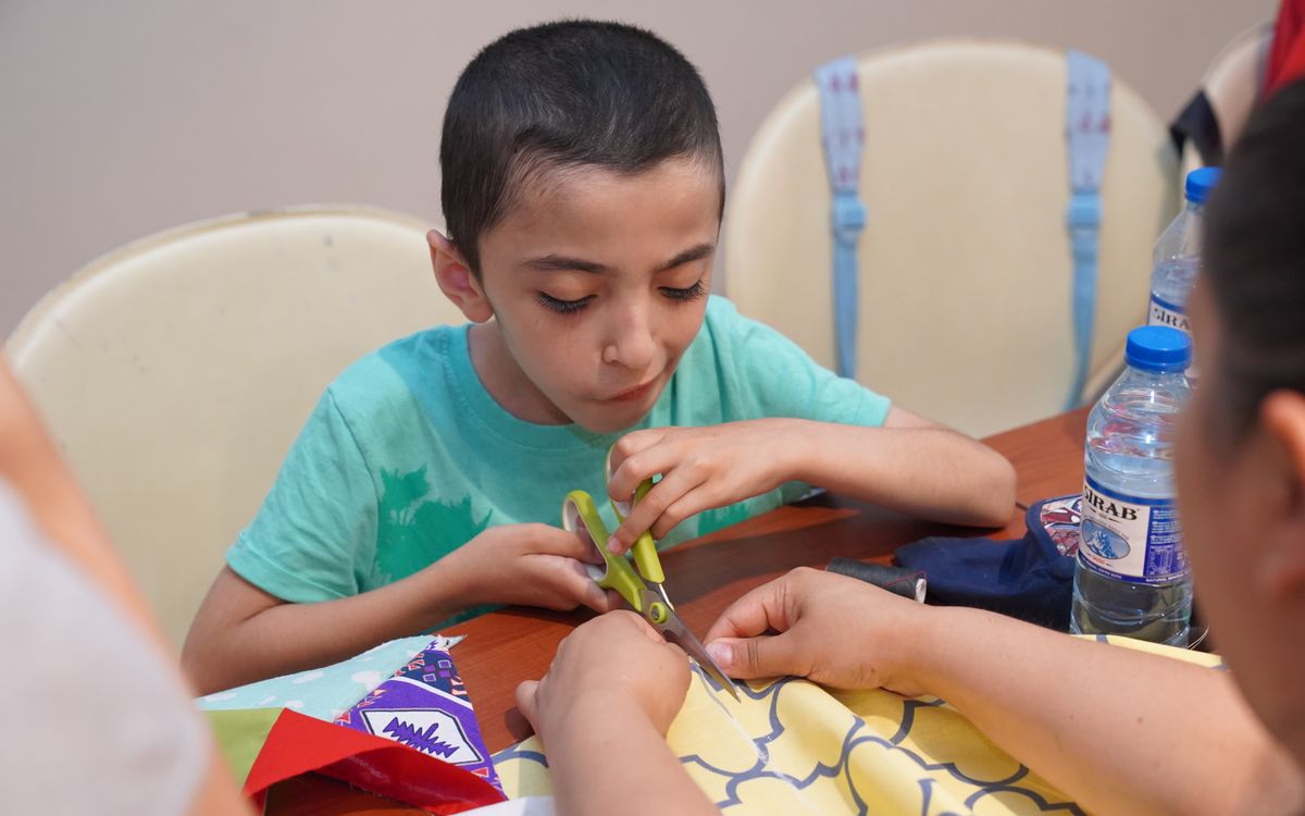 A child focused on crafting with scissors and colorful papers during an indoor arts and crafts session.