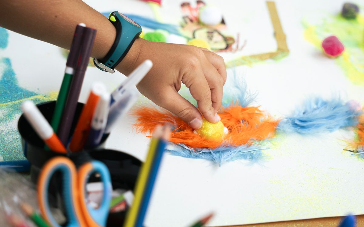 A child's hand creating a colorful art project with feathers and markers.