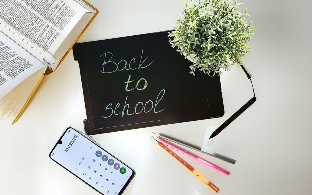 A bright, organized workspace for back to school featuring books, a phone, a plant, and stationery.