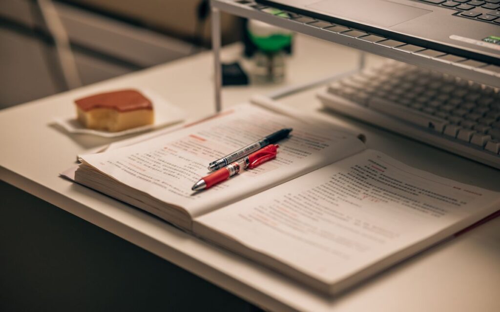 Open book with study notes, pens, and a laptop on a desk creating a focused study environment.