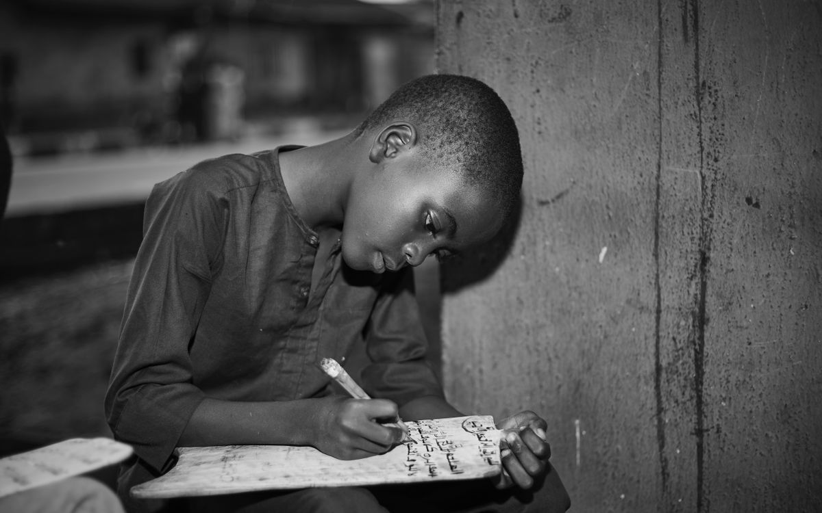 Black and white image of a young boy writing on a slate, focused and determined.