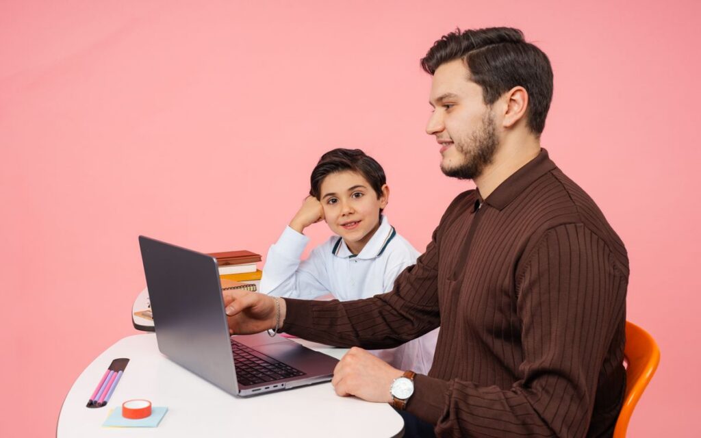 A teacher helps a student with laptop learning against a pink background in Yalova, Türkiye.