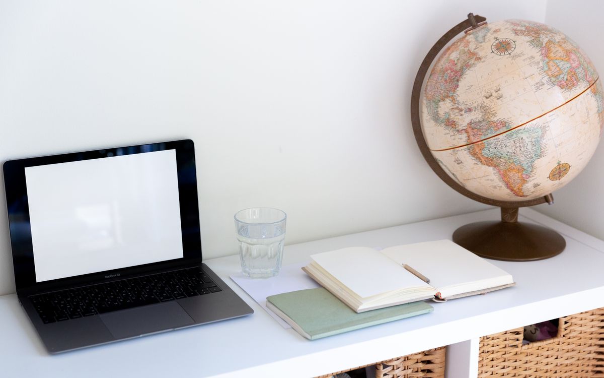 From above of empty screen of netbook placed near glass of water with opened white notepad near vintage globe at home