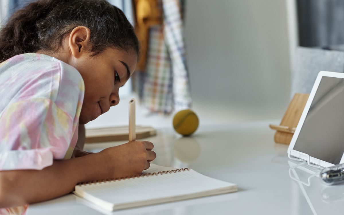 A young girl concentrating on homework at home using a tablet.