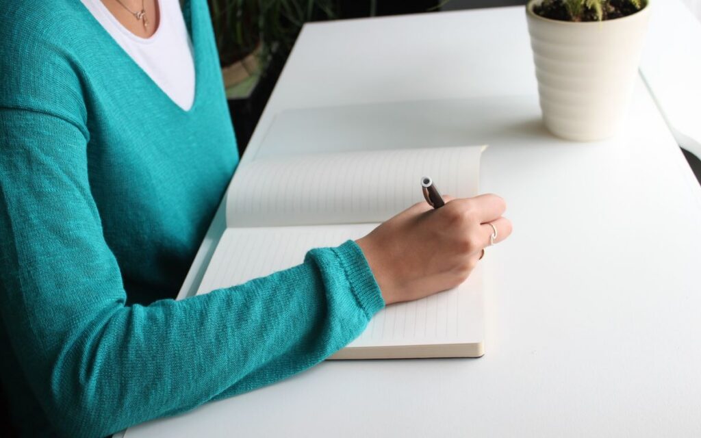 A woman writing in a notebook at a minimalist white desk indoors, emphasizing productivity.