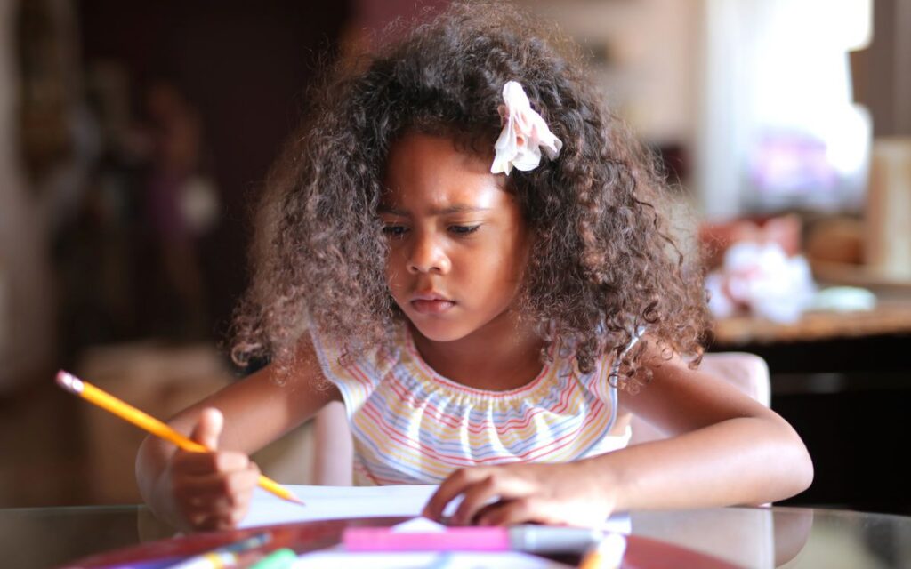 African American child focused on homework, writing with a pencil indoors.