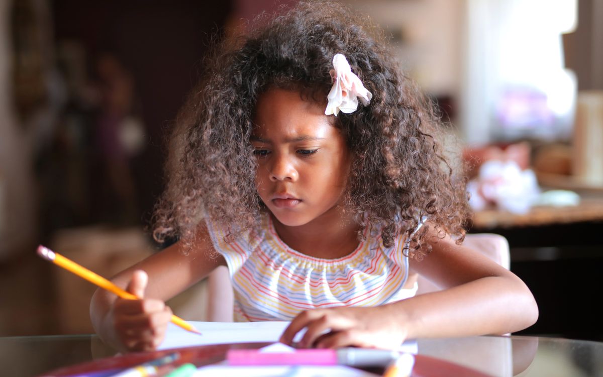 African American child focused on homework, writing with a pencil indoors.
