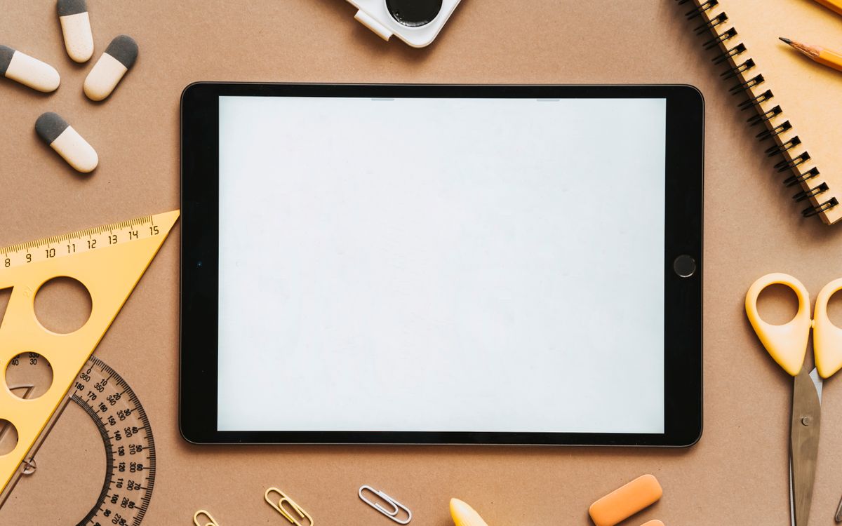 A flat lay featuring a tablet surrounded by school stationery items on a brown background.